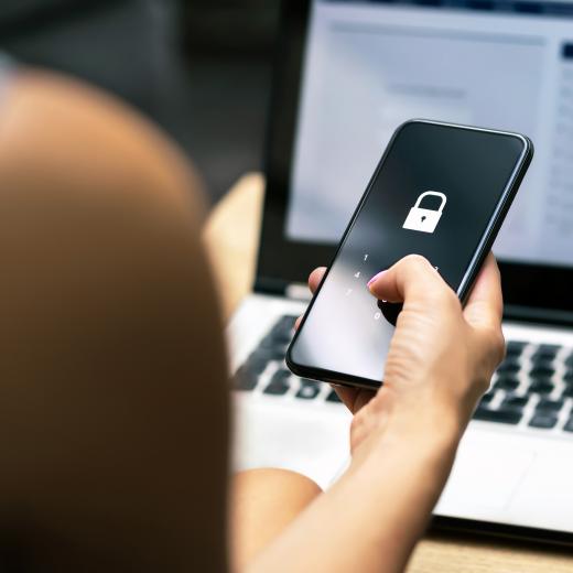 Person holding a cell phone in front of a laptop