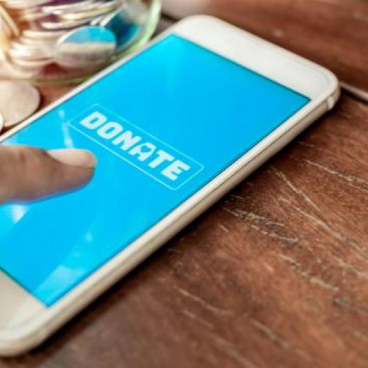 Someone's finger pushing on the word Donate on a mobile phone screen