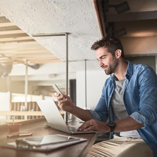 Man working on laptop and looking at mobile phone