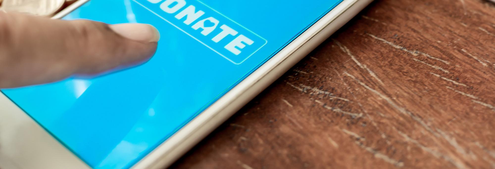 Someone's finger pushing on the word Donate on a mobile phone screen